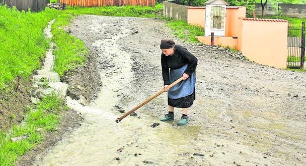 Pentru a opri şuvoiul ce riscă să îi intre în curte, o femeie încearcă să facă un dig micuţ